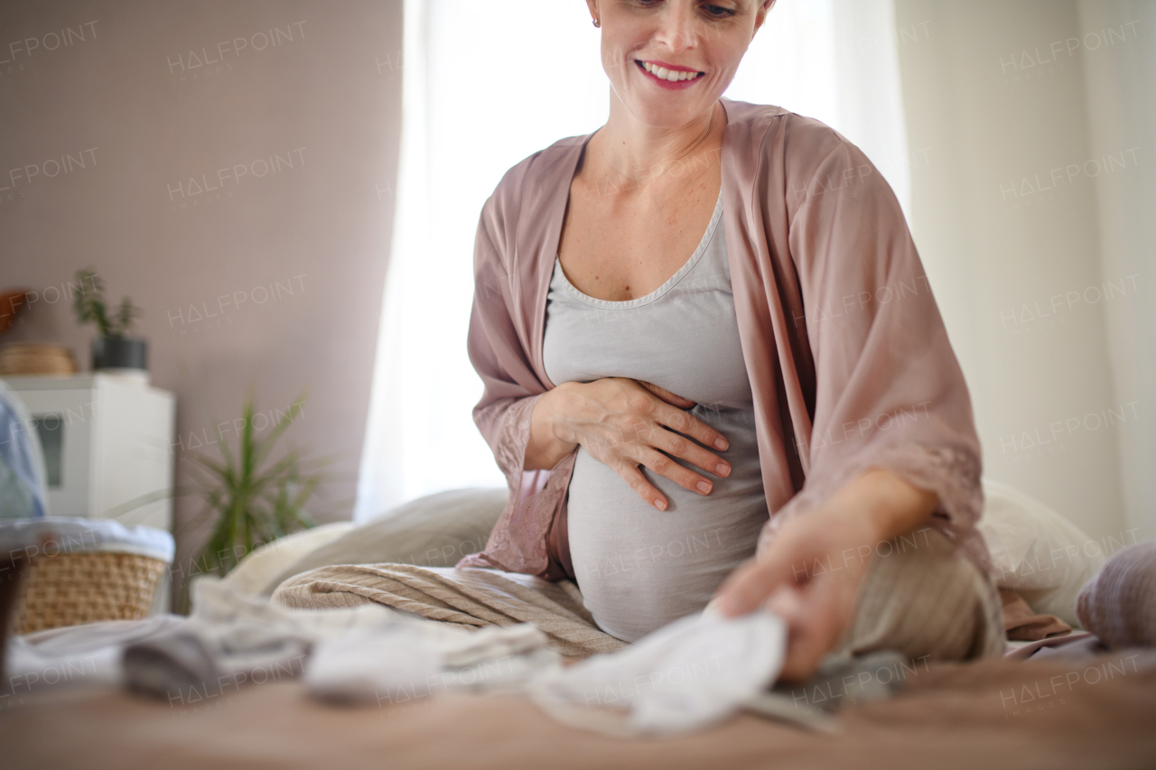 Happy pregnant woman looking at little baby clothes.