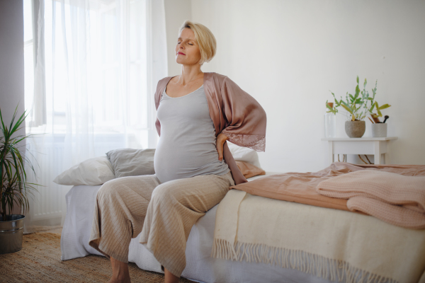 Tired pregnant woman sitting on her bed and resting.