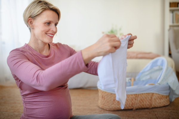 Happy pregnant woman looking at little baby clothes.