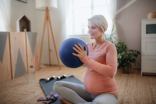 Pregnant woman doing exercises with ball in the apartment.