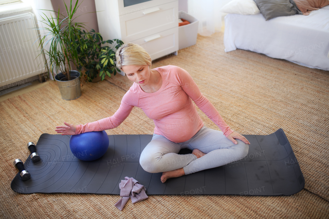 Pregnant woman doing exercises with ball in the apartment.