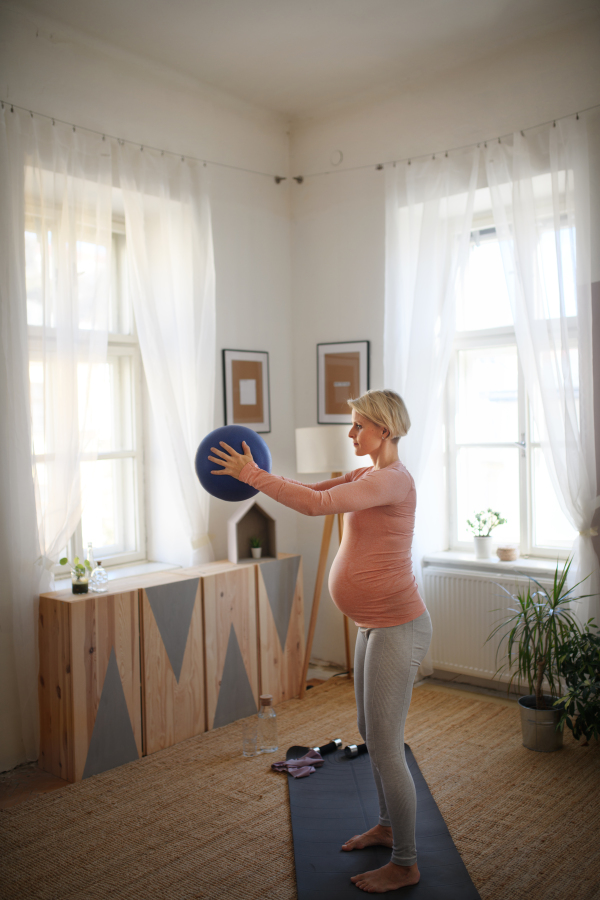 Pregnant woman doing exercises with ball in the apartment.