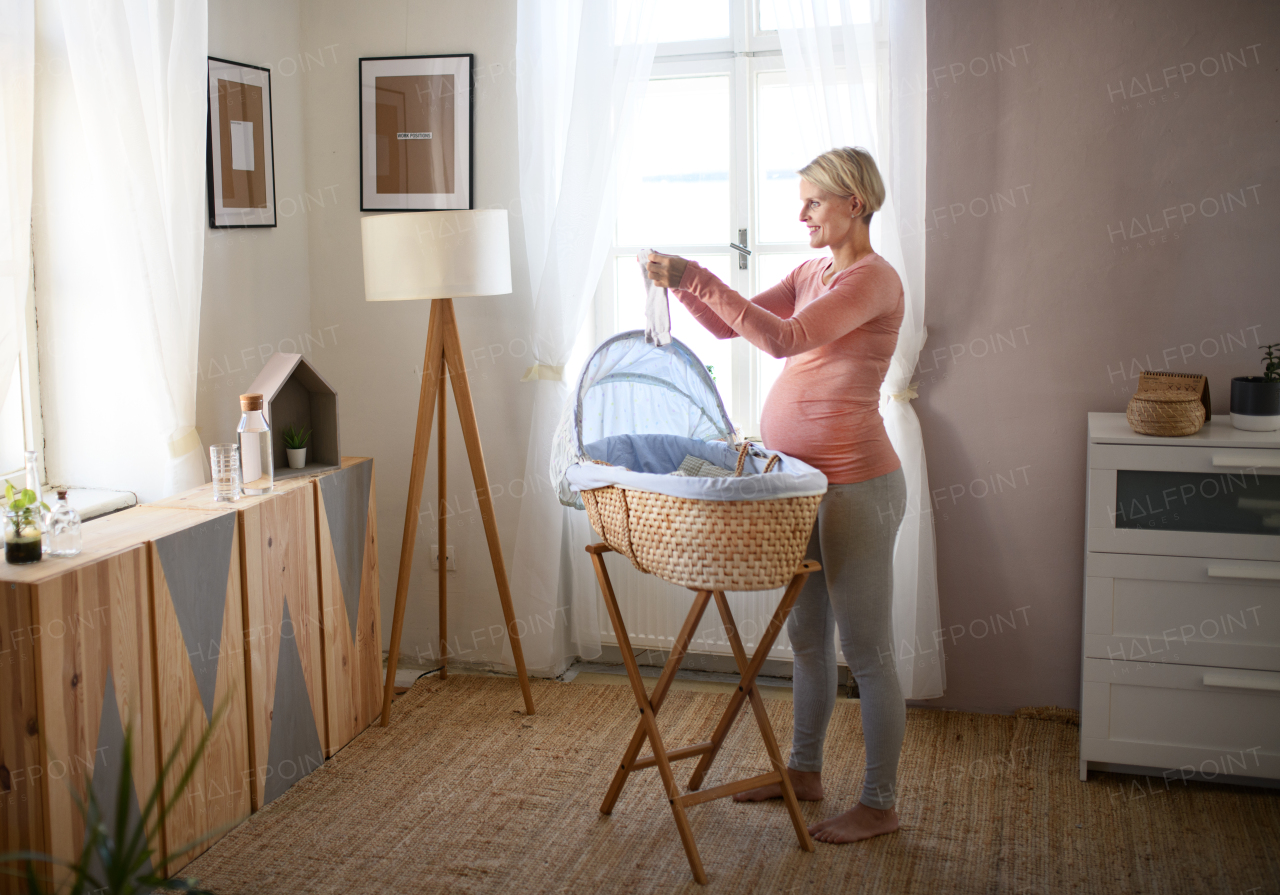 Happy pregnant woman looking at little baby clothes.