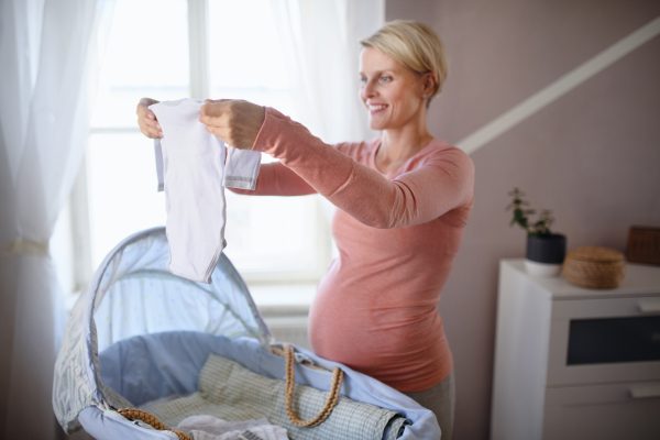 Happy pregnant woman looking at little baby clothes.