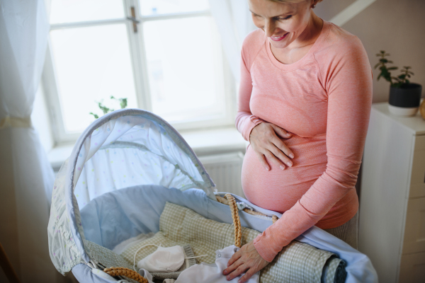 Happy pregnant woman looking at little baby clothes.