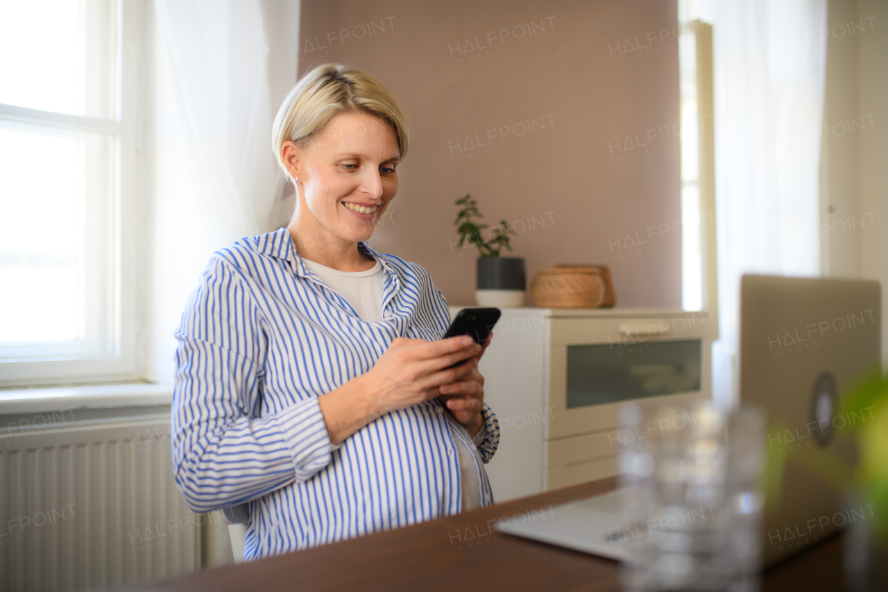 Pregnant woman having home office, scrolling her smartphone.