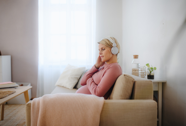 Pregnant woman sitting in a bed, listening music and enjoying time for herself.