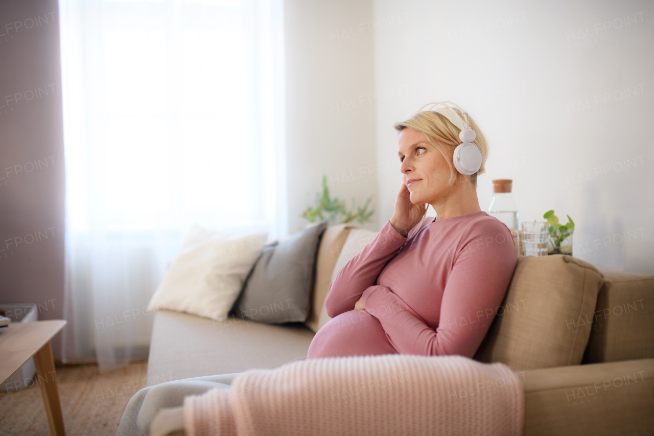 Pregnant woman sitting in a bed, listening music and enjoying time for herself.