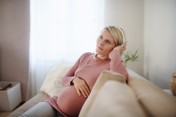 Pregnant woman sitting on a sofa, listening music and enjoying time for herself.