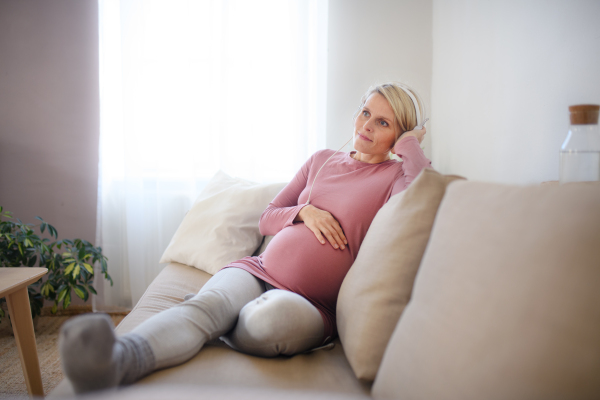 Pregnant woman sitting in a bed, listening music and enjoying time for herself.