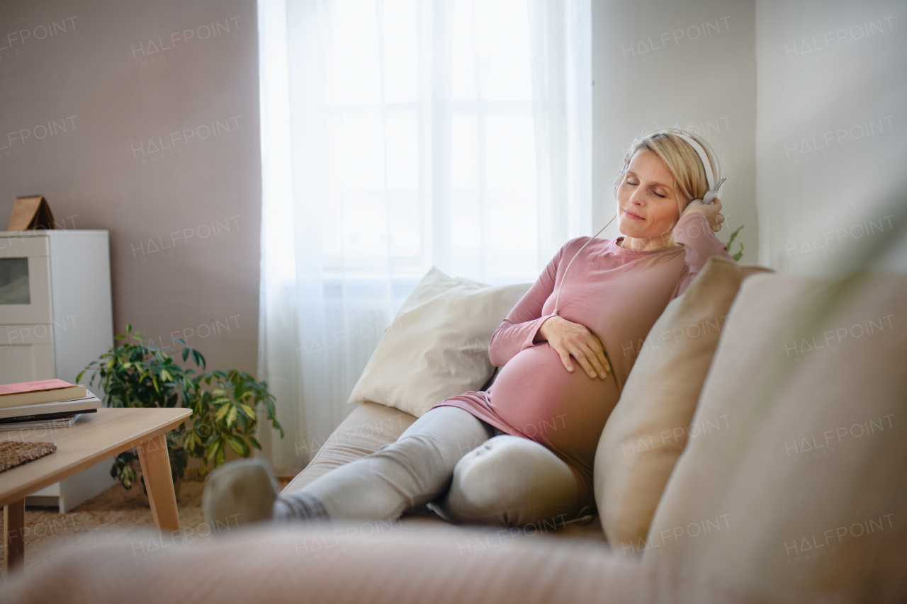 Pregnant woman sitting in a bed, listening music and enjoying time for herself.