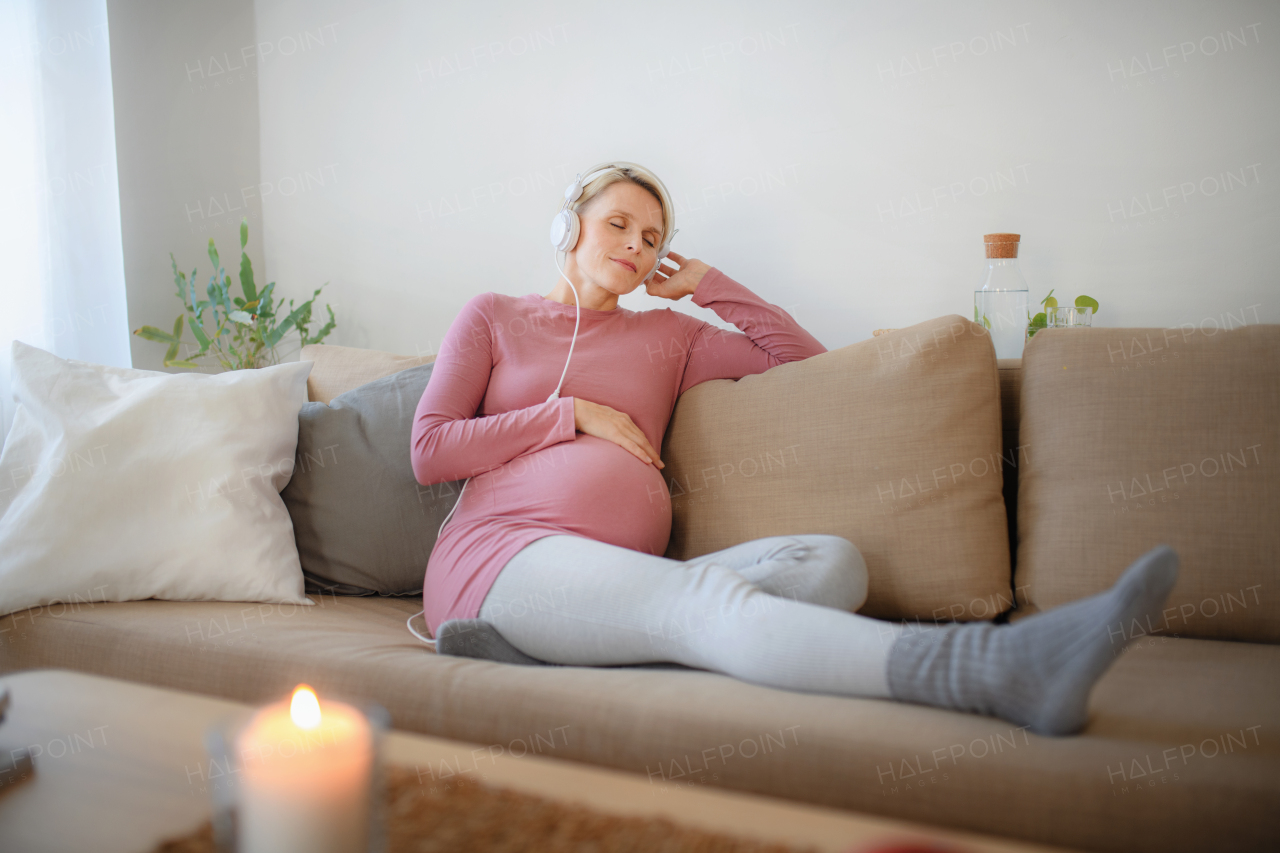 Pregnant woman sitting in a bed, listening music and enjoying time for herself.