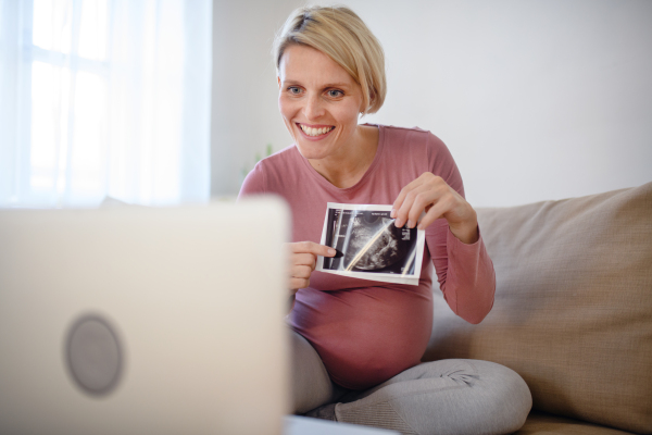 Pregnant woman showing ultrasound photo of a baby to webcam.