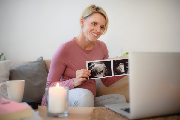 Pregnant woman showing ultrasound photo of a baby to webcam.