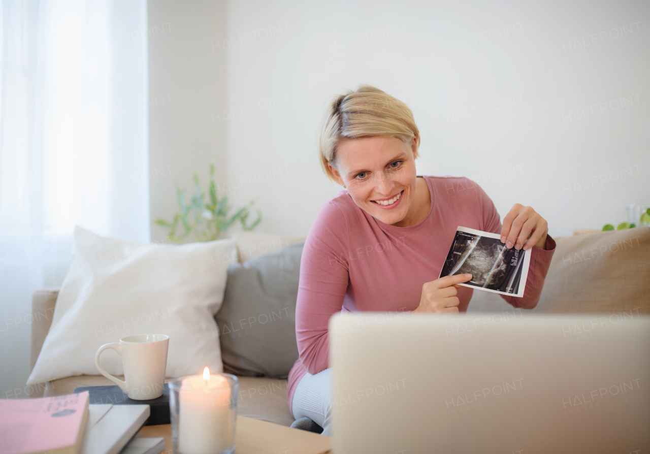 Pregnant woman showing ultrasound photo of a baby to webcam.