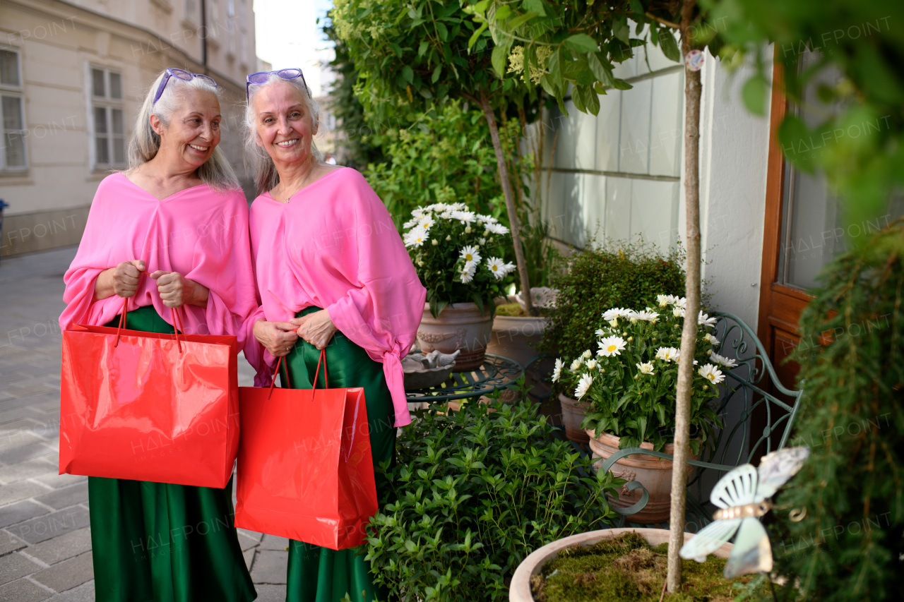 Senior women twins in colourful clothes in the city, shopping.