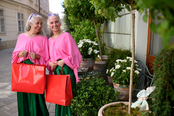 Senior women twins in colourful clothes in the city, shopping.