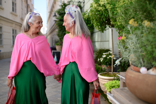 Senior women twins in colourful clothes in the city, shopping.