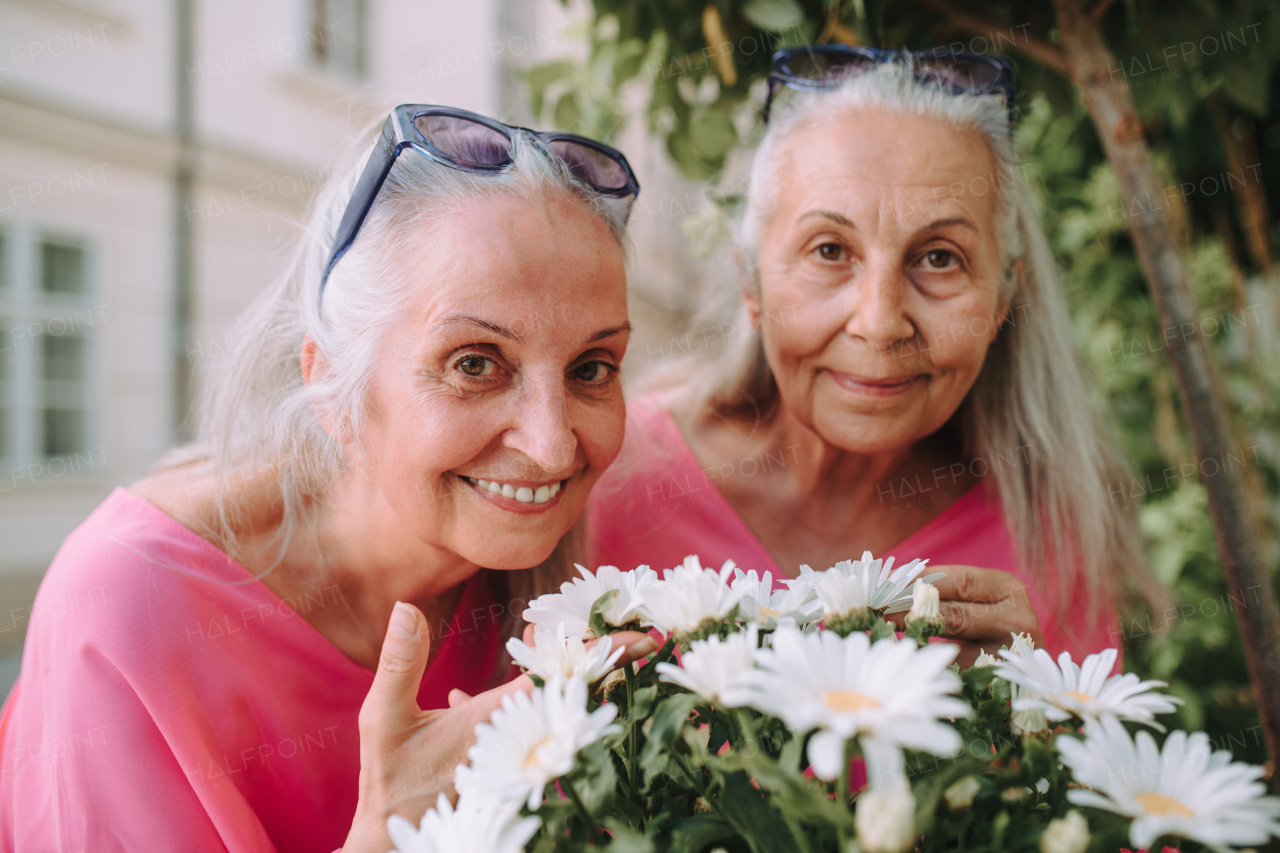 Portrait of a senior women twins with flowers outdoor in city park.