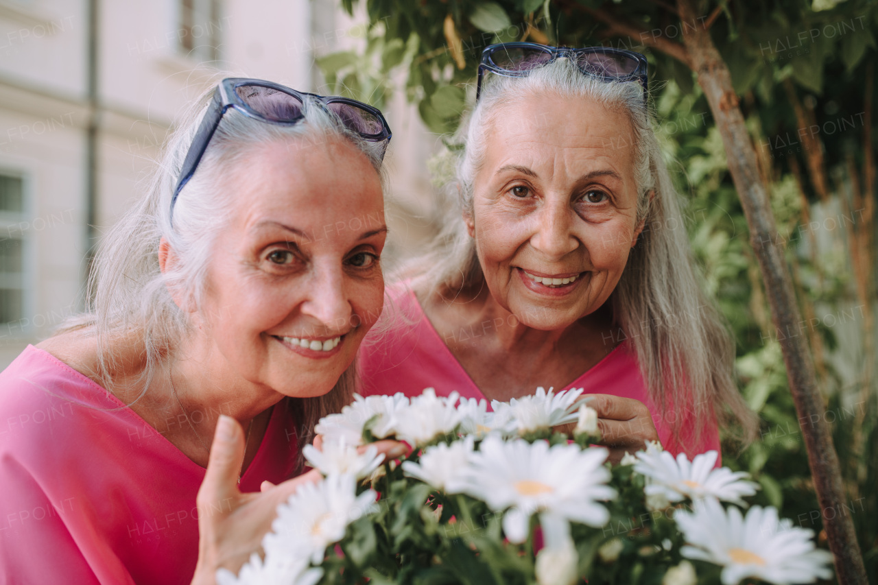 Portrait of a senior women twins with flowers outdoor in city park.