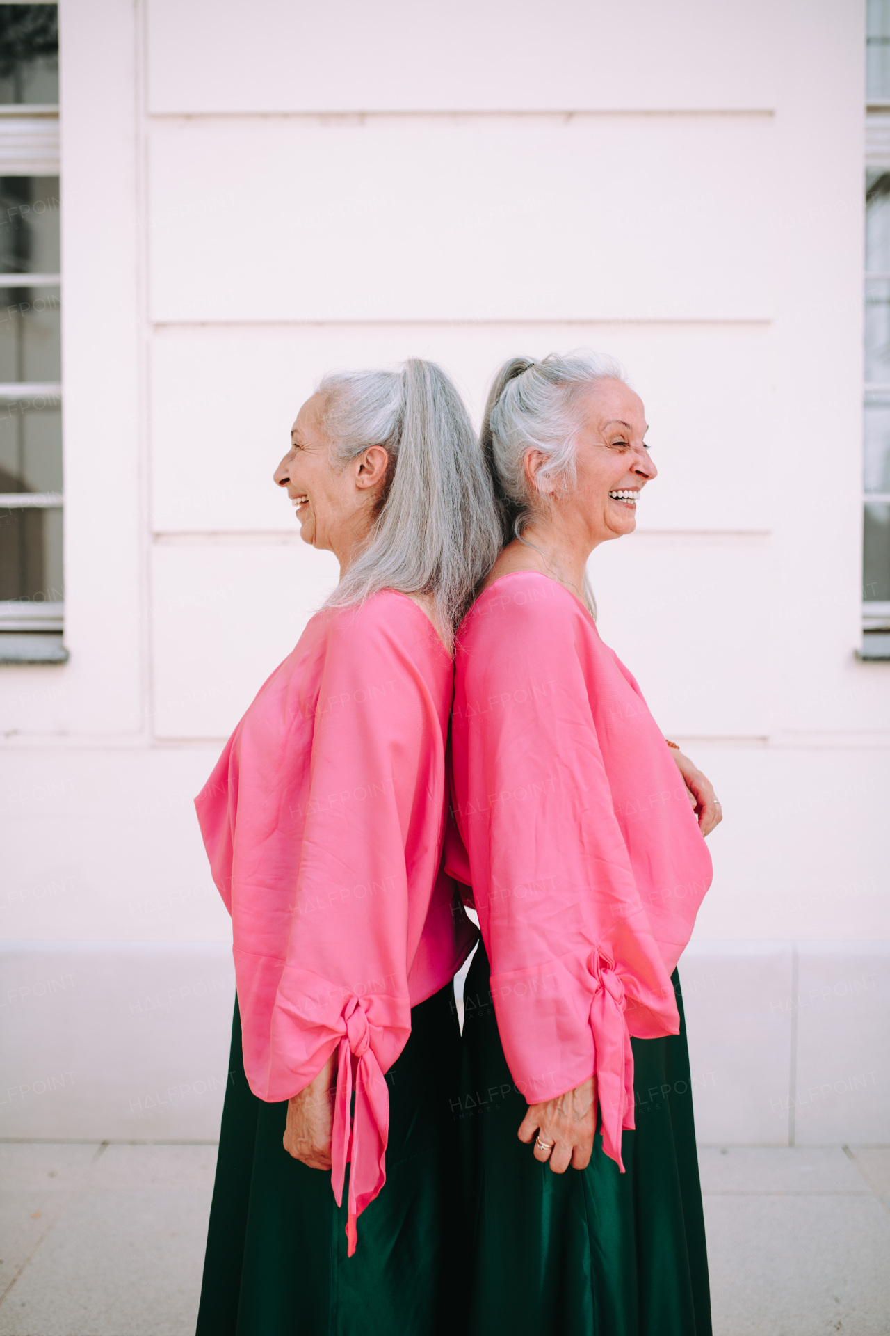 Side view of senior women, twins,in same clothes standing back to back, outdoor in a city.