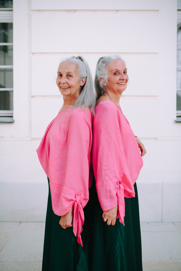 Side view of senior women, twins,in same clothes standing back to back, outdoor in a city.