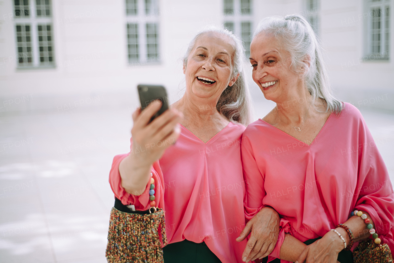 Senior women twins outdoors in a city taking selfie.