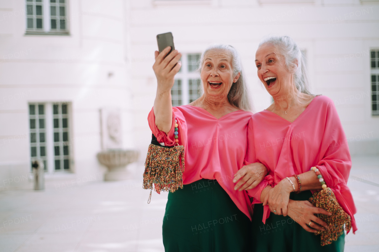 Senior women twins outdoors in a city taking selfie.