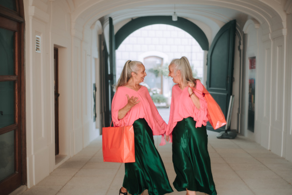 Happy senior women twins in colourful clothes in the city, shopping.