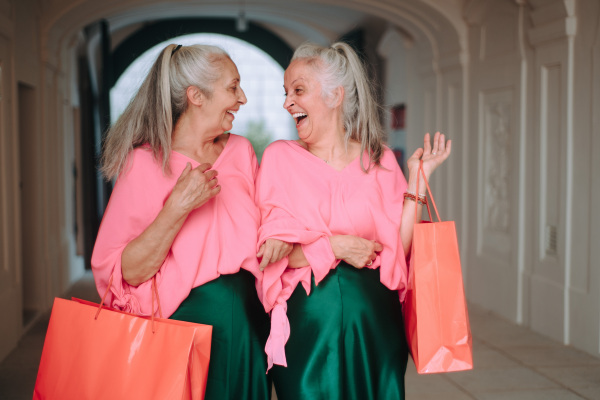 Happy senior women twins in colourful clothes in the city, shopping.