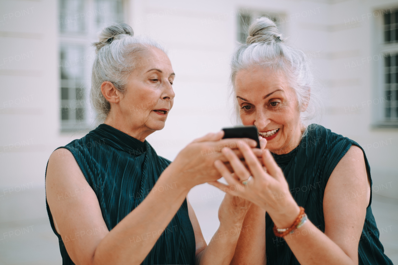 Senior women twins outdoors in city checking a smartphone.