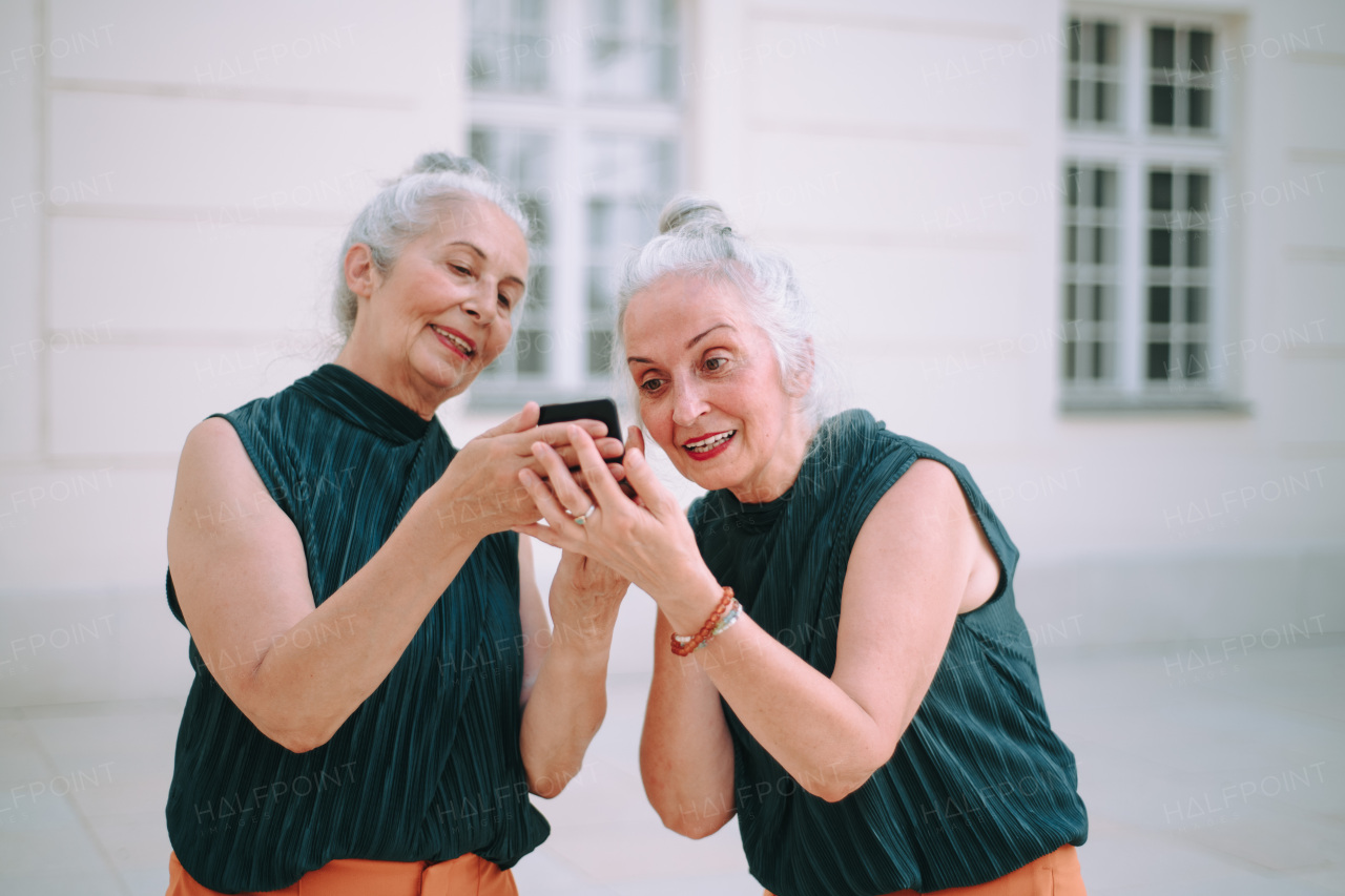 Senior women twins outdoors in city checking a smartphone.