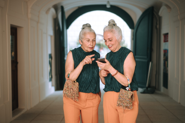 Senior women twins outdoors in city checking a smartphone.