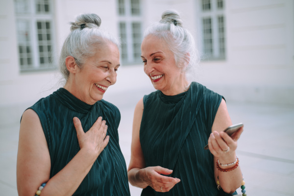 Happy senior twins in same clothes talking and walking in a city.