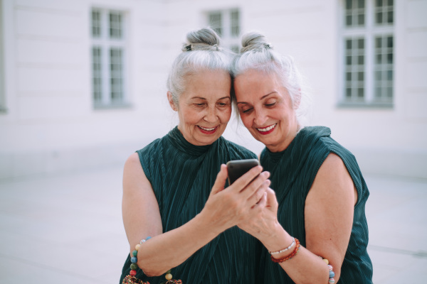 Senior women twins outdoors in city checking a smartphone.