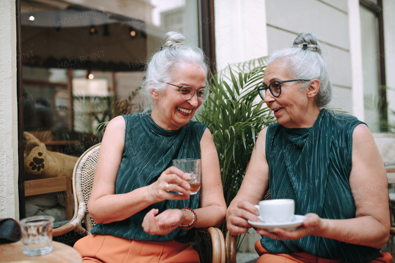 Happy senior women twins having a coffee break in city, smiling and talking.