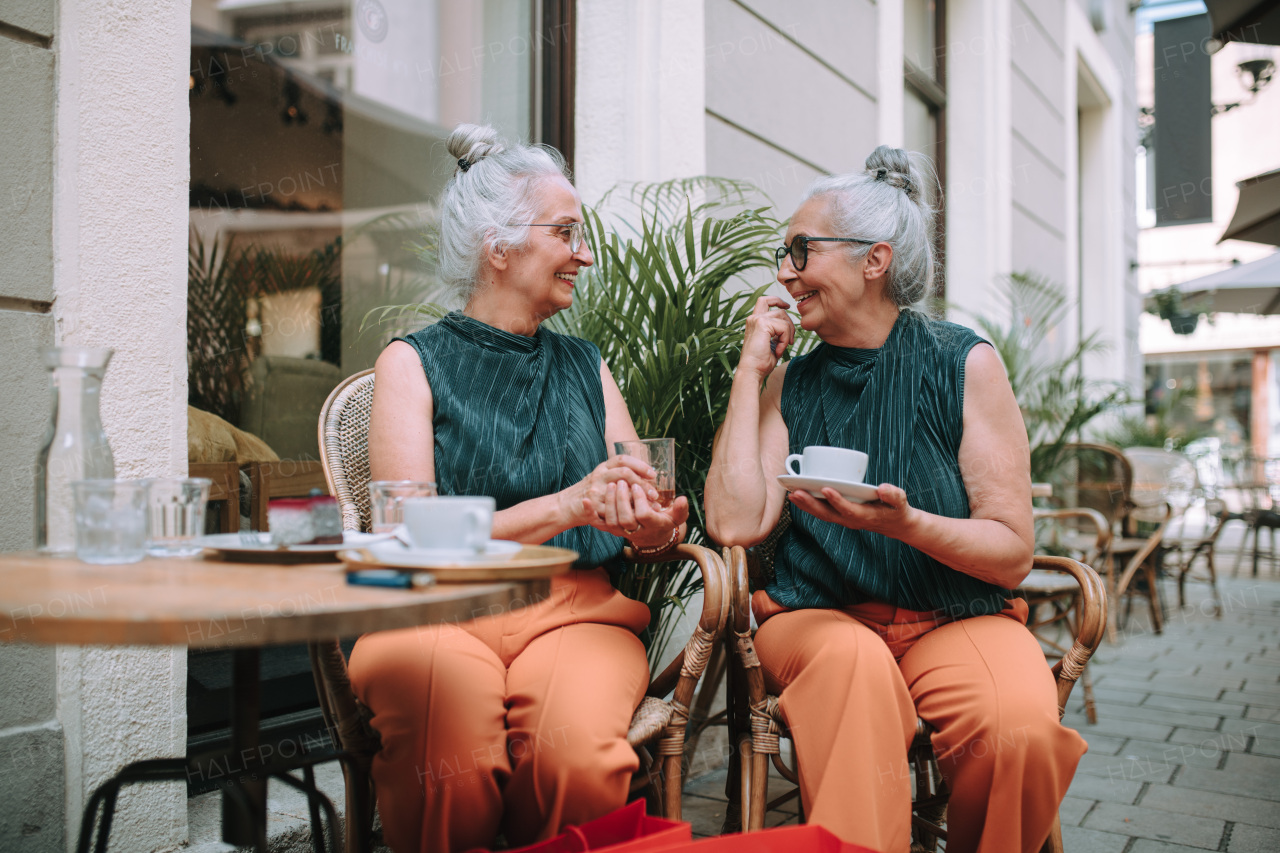 Happy senior women twins having a coffee break in city, smiling and talking.