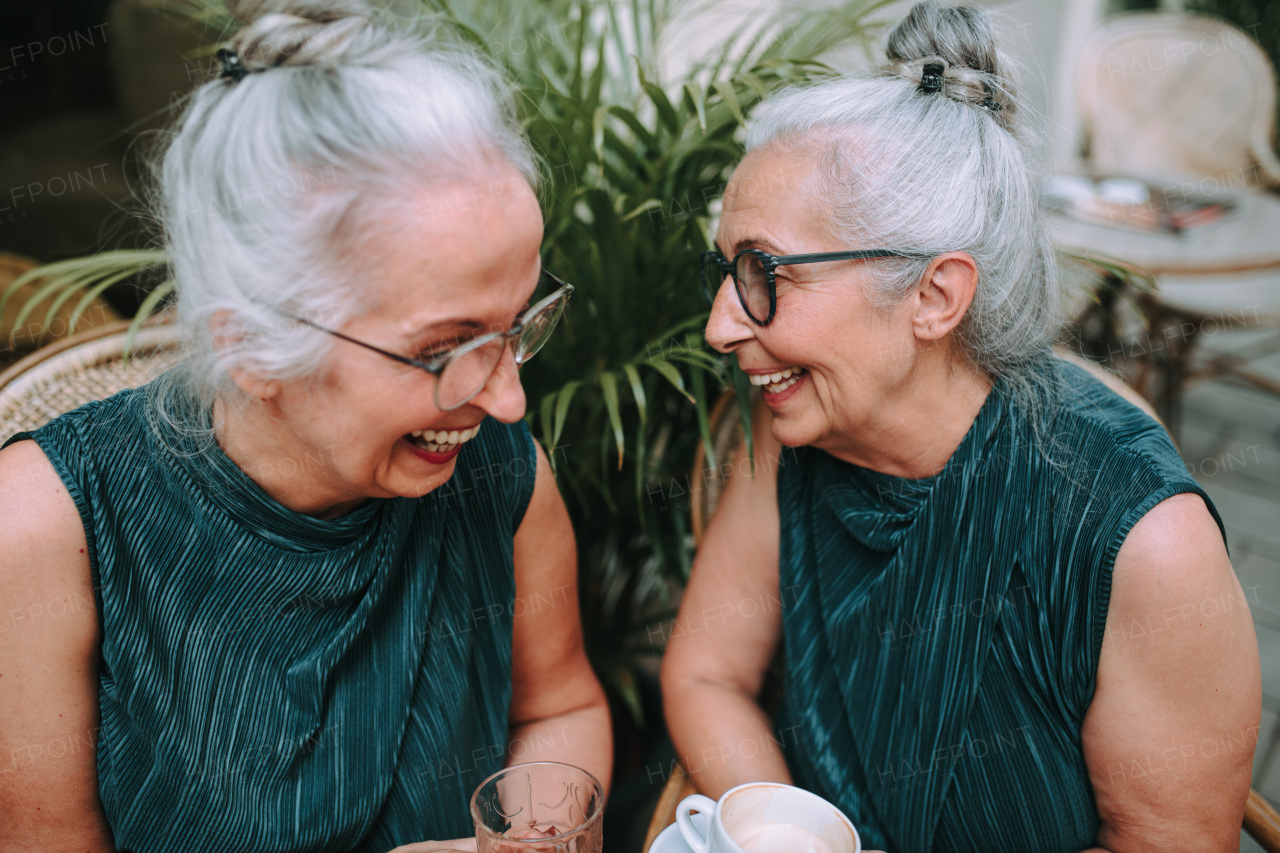 Happy senior women twins having a coffee break in city, smiling and talking.