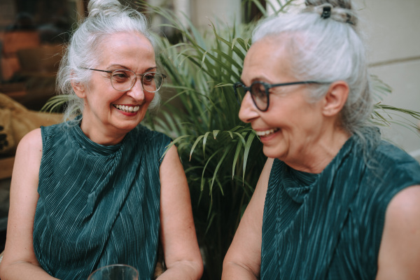 Happy senior women twins having a coffee break in city, smiling and talking.