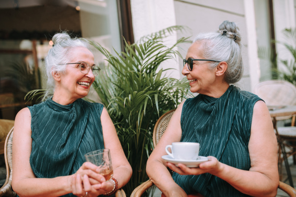 Happy senior women twins having a coffee break in city, smiling and talking.