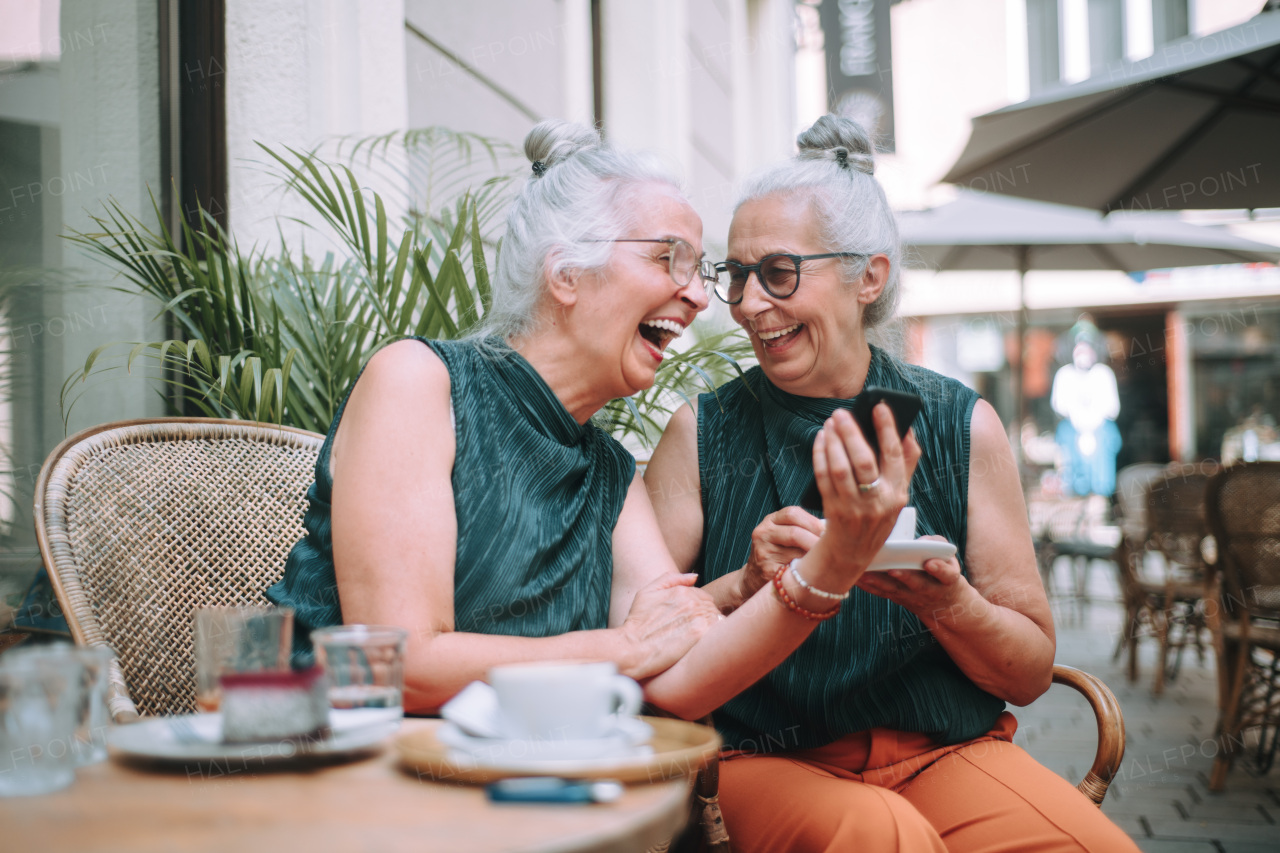 Happy senior women twins having a coffee break in city, smiling and talking.