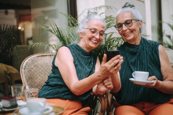 Happy senior women twins having a coffee break in city, smiling and talking.