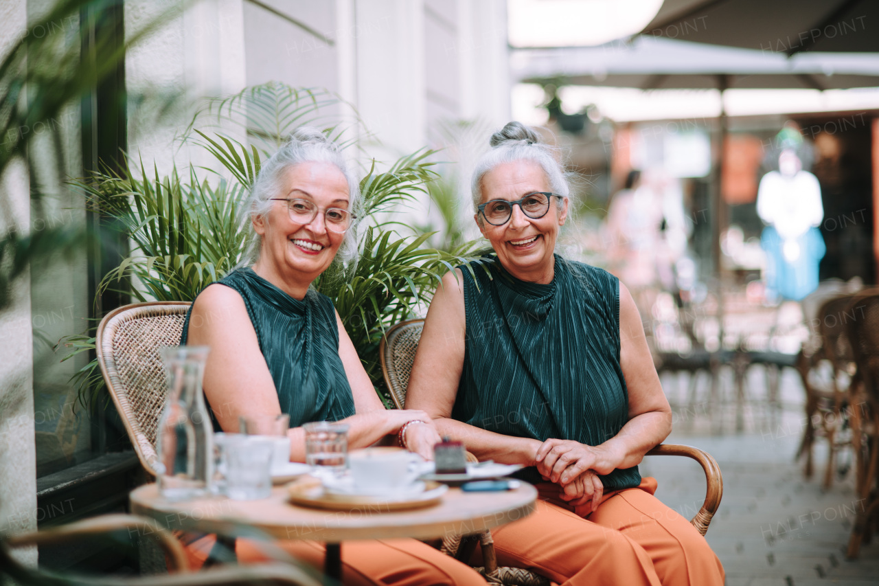 Happy senior women twins having a coffee break in city, smiling and talking.