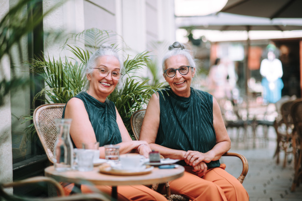 Happy senior women twins having a coffee break in city, smiling and talking.