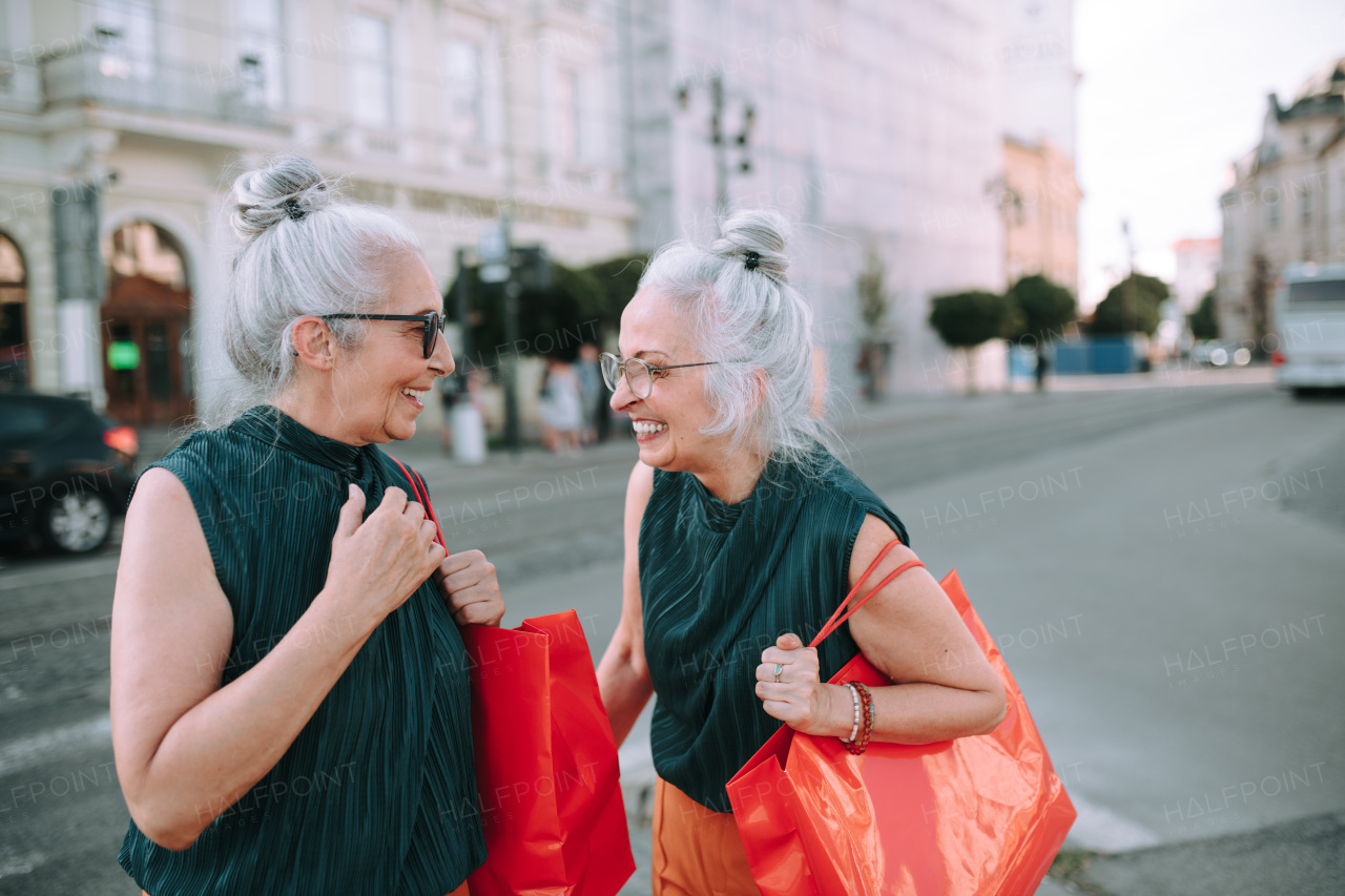 Happy senior twins in same clothes walking in a city, returning from shopping.