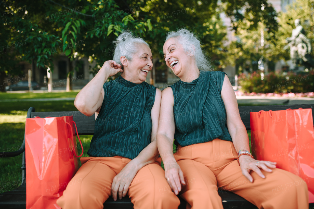 Happy senior sister, twins sitting in a city park and resting after shopping.