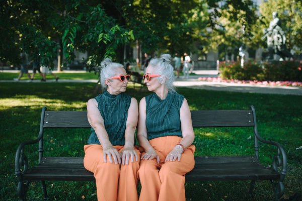 Happy senior sister, twins sitting in a city park and resting after shopping.