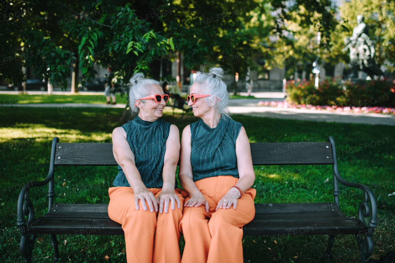 Happy senior sister, twins sitting in a city park and resting after shopping.