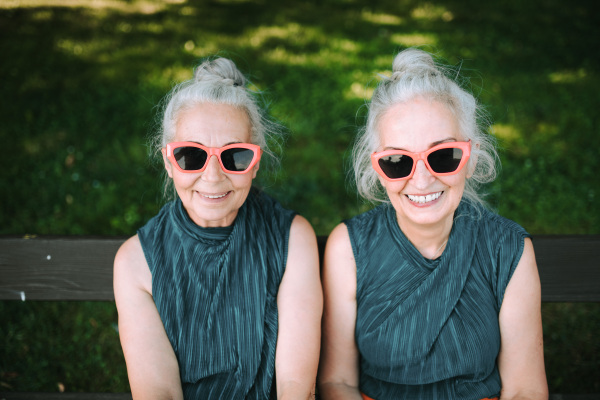 High angle view of happy senior women, twins in same clothes, smiling and posing in a city park.