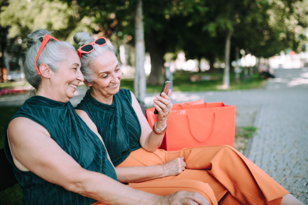 Senior women twins outdoors in city checking a smartphone.